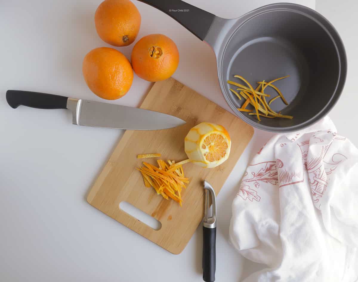 Sliced orange peel on a cutting board next to a peeled orange.