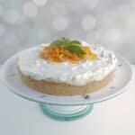 Orange creamsicle cheesecake on a cake pedestal with candied orange peel and mint leaves garnishing the top in the center.