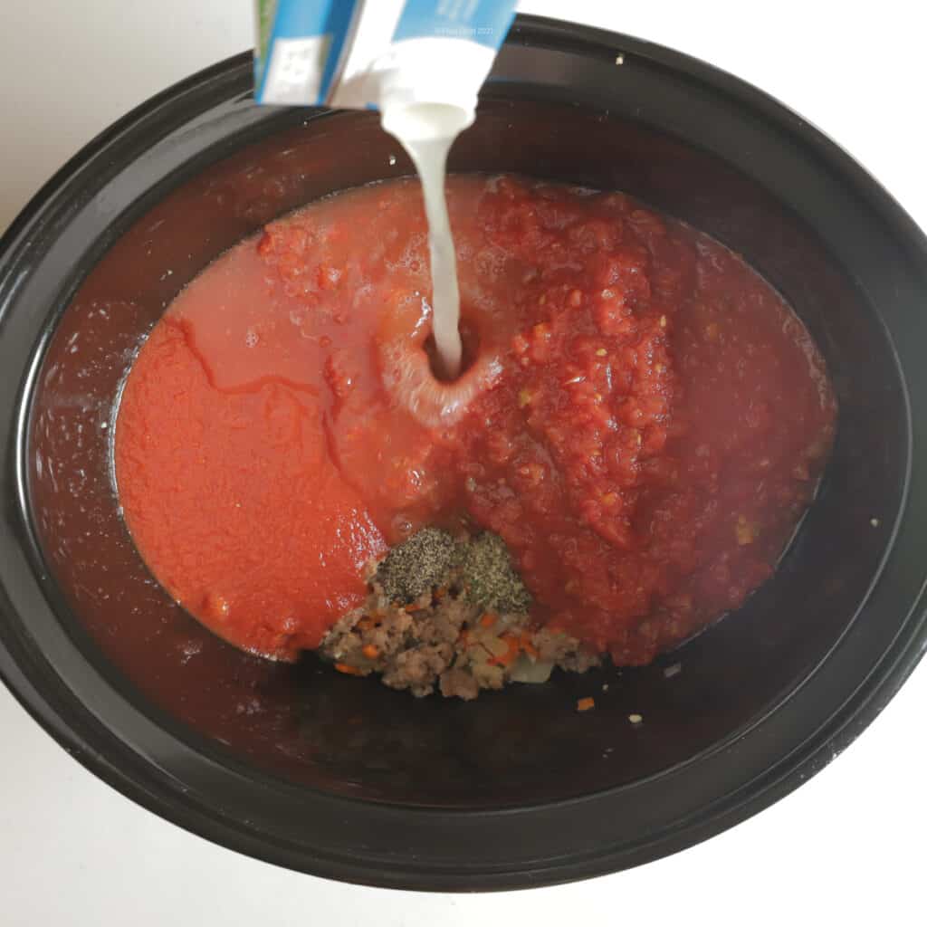 Chicken broth pouring into pot with meat, vegetables, tomatoes and spices