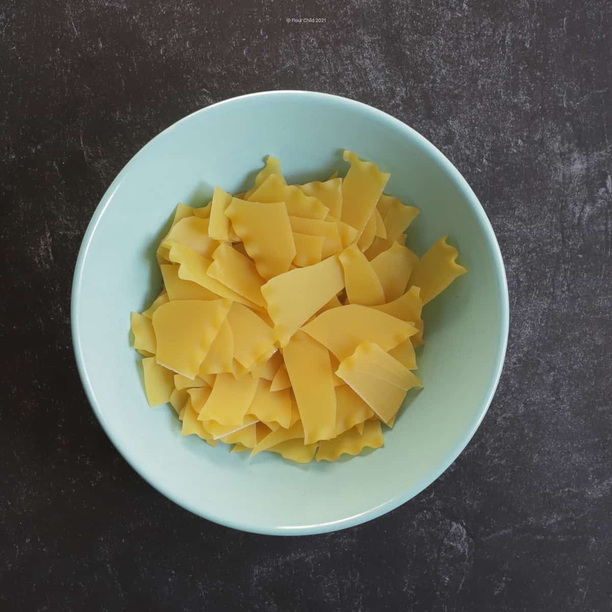 Uncooked lasagna noodles broken into 1 inch pieces, sitting in blue bowl