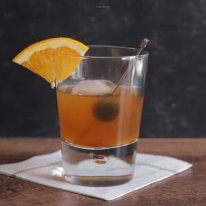 An amaretto sour cocktail in a small glass with orange slice and cherry