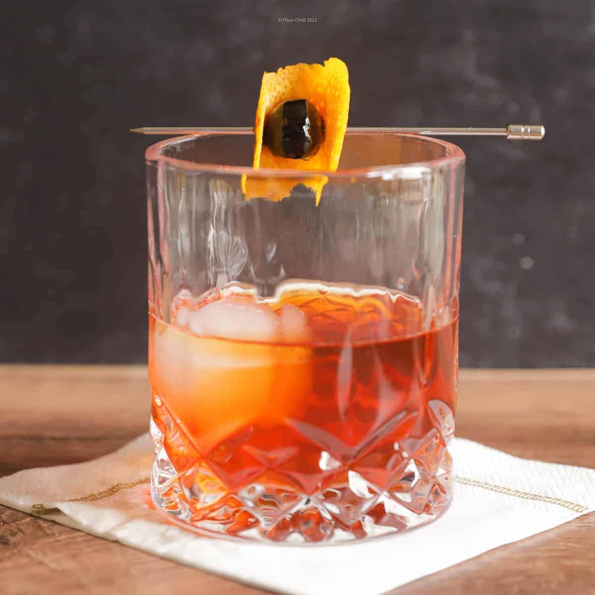 An old fashioned in a lowball glass with a large ice cube and an orange  peel