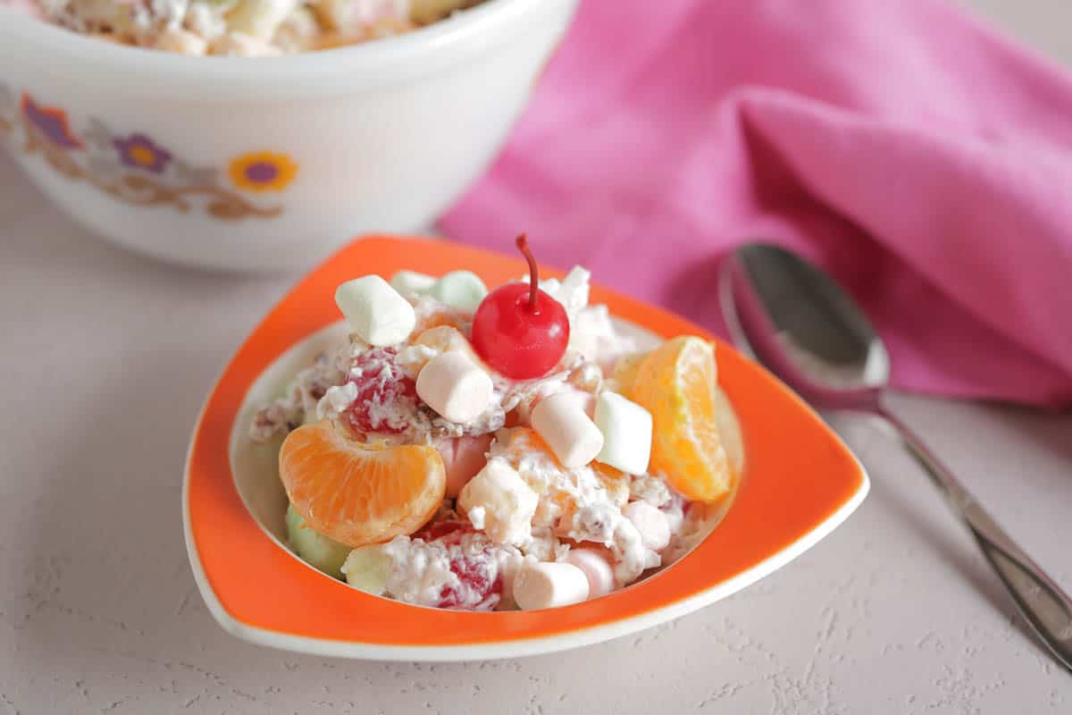 A serving size dish of ambrosia salad in a mid century style orange bowl
