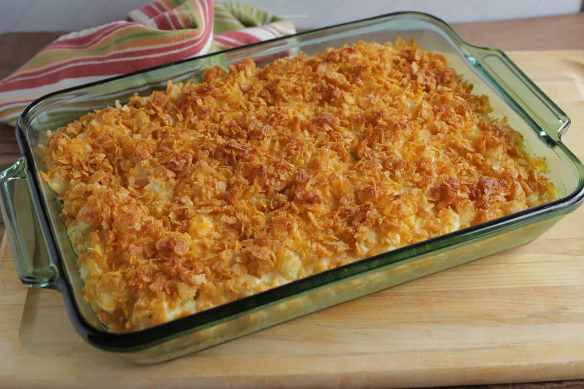 Cheesy potato casserole topped with corn flakes in a green casserole dish, just taken hot from the oven.