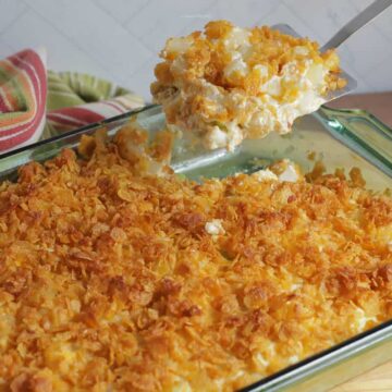 Potato casserole in a green casserole dish, with a scoop being lifted out with a spatula for serving.