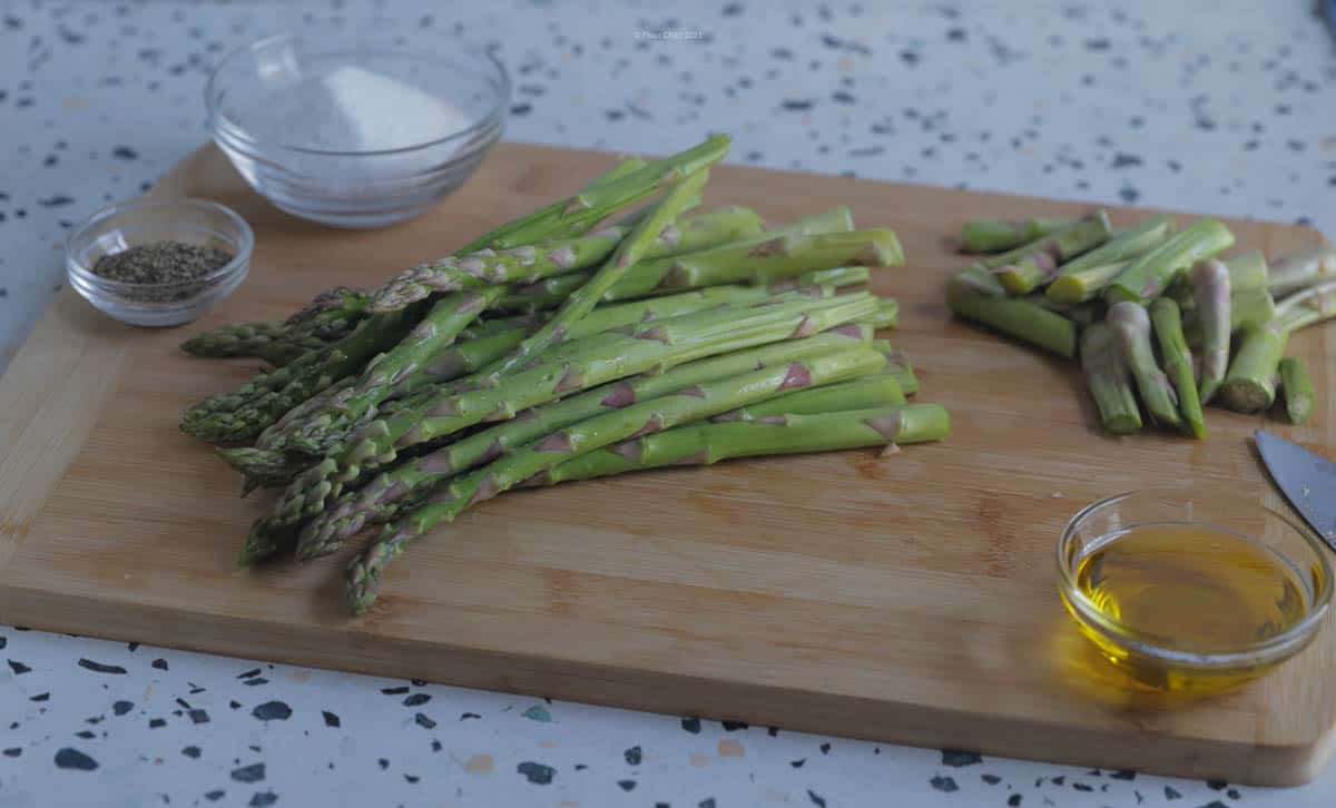 A bunch of asparagus on a cutting board, with the bottom tips cut off about 1 and a half inches