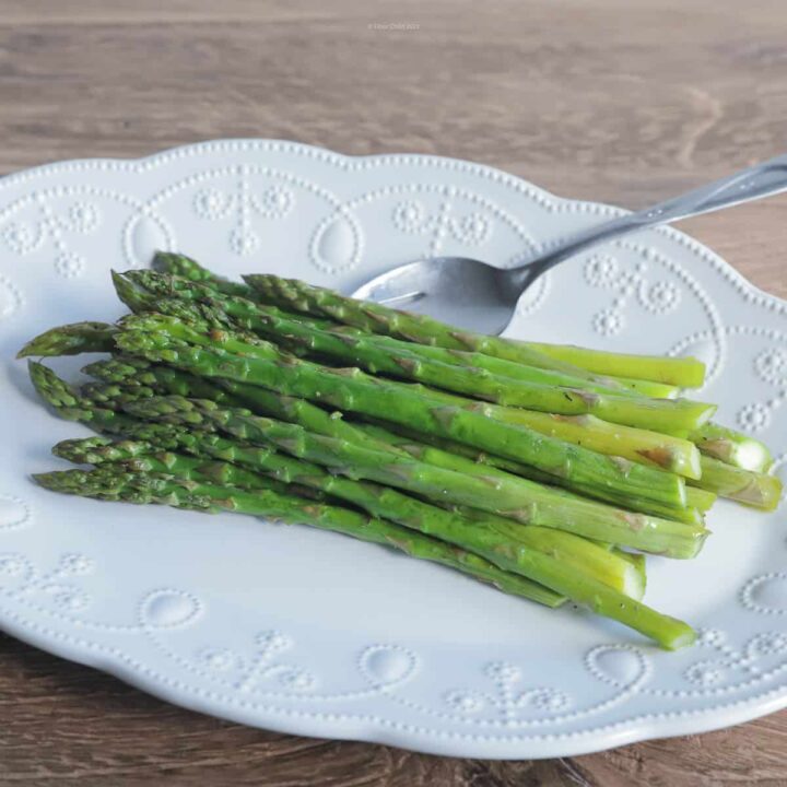 Fresh roasted asparagus on a white serving plate, with a serving fork resting on the side.