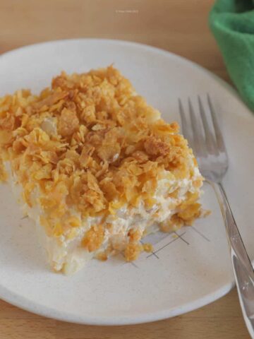 Slice of cheesy potato casserole on a mid century plate with a fork and napkin.