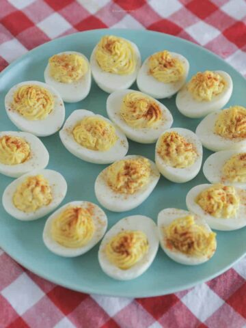 A dozen deviled eggs on a blue batter, sitting on a red-checkered table cloth.