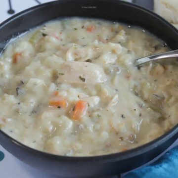 A blue bowl of cream of chicken and wild rice soup with a spoon in it.