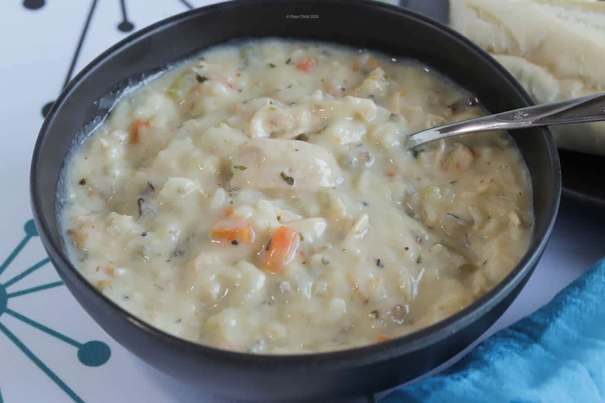 A blue bowl of cream of chicken and wild rice soup with a spoon in it.