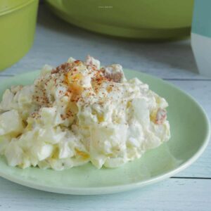 A serving of classic potato salad on a green salad plate. Paprika is sprinkled on top.