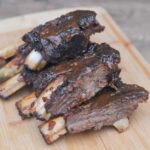 A stack of grilled beef ribs on a wooden cutting board.