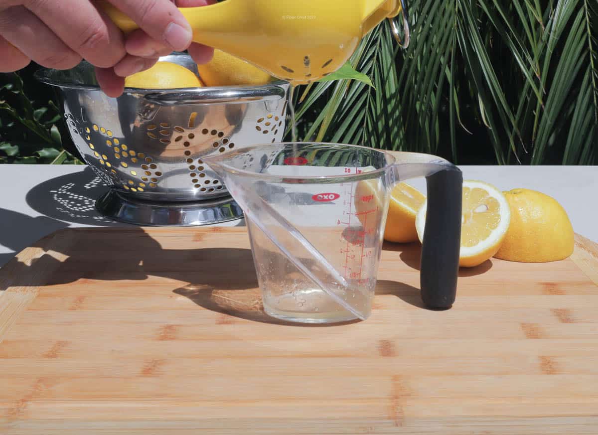 A lemon squeezing tool held over a measuring cup, with Lemon juice flowing into it.