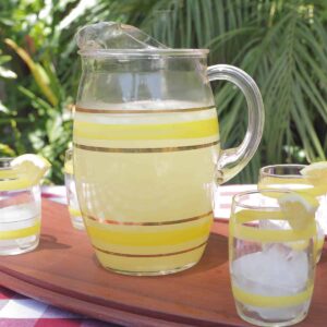 A pitcher of old fashioned lemonade ready to pour into the 4 surrounding glasses that are garnished with a lemon wedge.