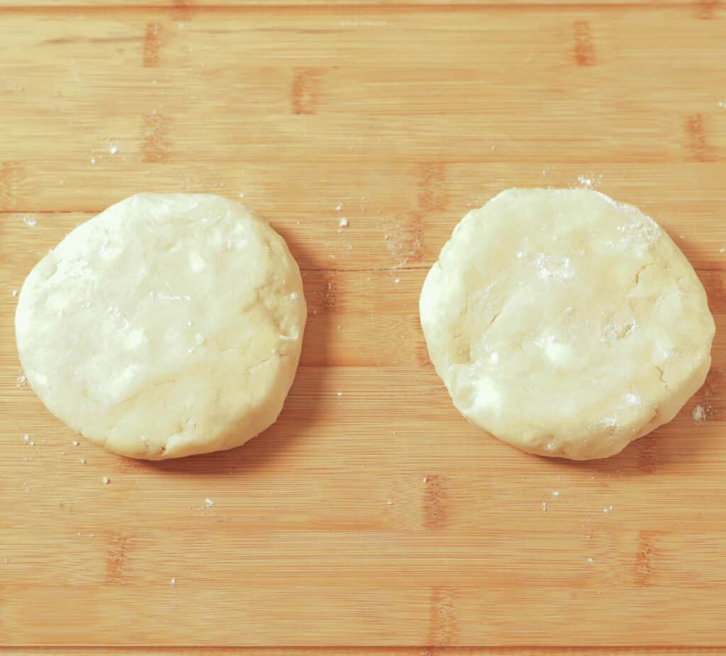 Two discs of dough on a rolling surface ready to be rolled into pie crust.