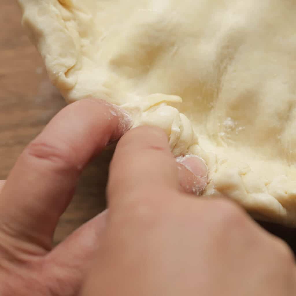 Using two hands to crimp the edges of pie dough