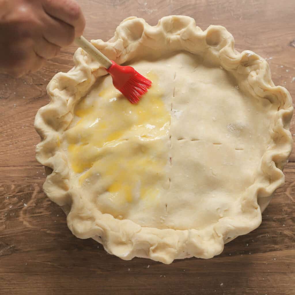 A red basting brush basting the top of the pie crust with egg wash
