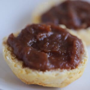 Apple butter on top of a fluffy biscuit on a white plate.