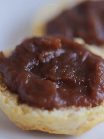Apple butter on top of a fluffy biscuit on a white plate.