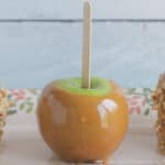 Carmel apple with a wooden stick set on a piece of parchment paper, ready to serve.