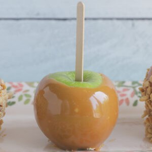 Carmel apple with a wooden stick set on a piece of parchment paper, ready to serve.