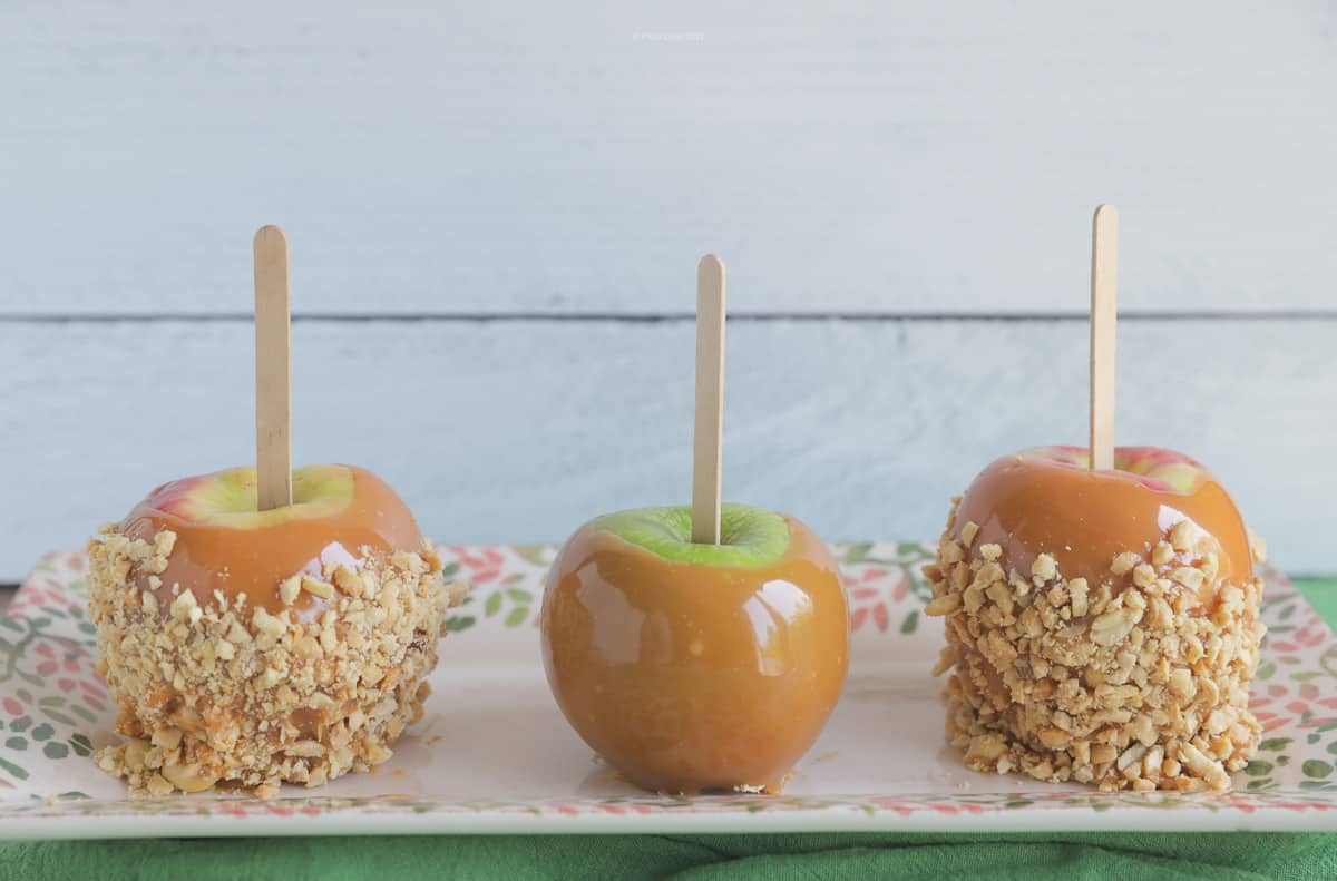 One caramel apple between two taffy apples on an oblong serving plate.