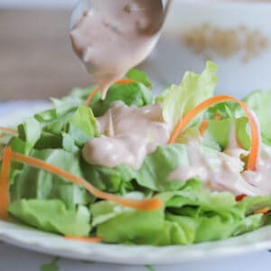A garden salad on a white salad plate, with Thousand Island dressing being spooned over it.
