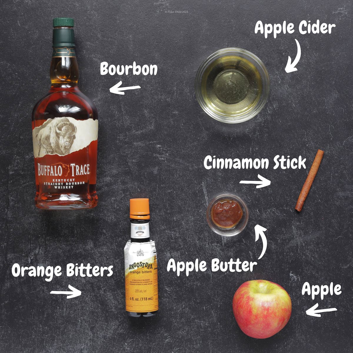 A list of ingredients for an apple butter old fashioned that includes a bottle of bourbon, orange bitters, apple, cinnamon stick and apple cider.