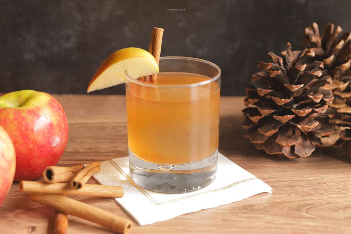 An apple butter old fashioned cocktail in a tumbler with apples and other fall related items