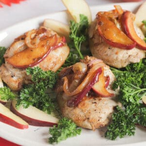 Boneless apple cider pork chops on a serving platter, topped with cooked apples and surrounded with fresh sprigs of parsley.