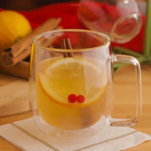 Hot Toddy cocktail in a clear mug with a lemon wheel and 2 small cranberries for garnish