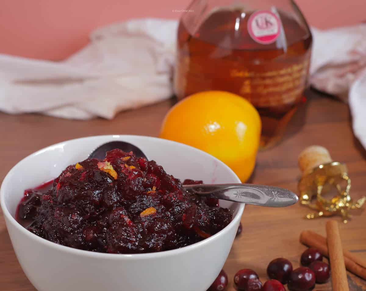 White bowl of cranberry sauce with orange zest with bottle of bourbon in background