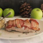 Pork tenderloin with bacon on top, sitting on a mid century serving platter with a side of French apple sauce.