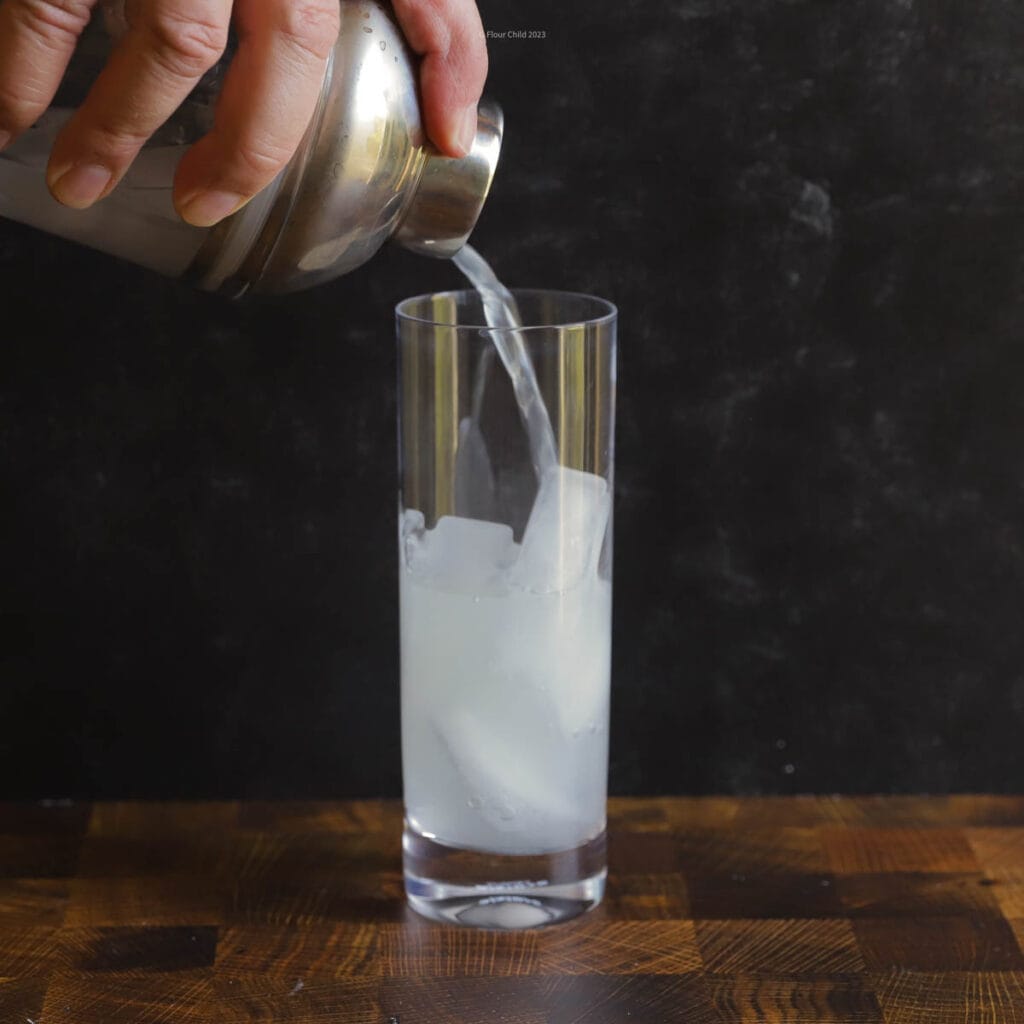 The process steps of pouring lime juice, rum and sugar into a cocktail shaker and straining into a collins glass.