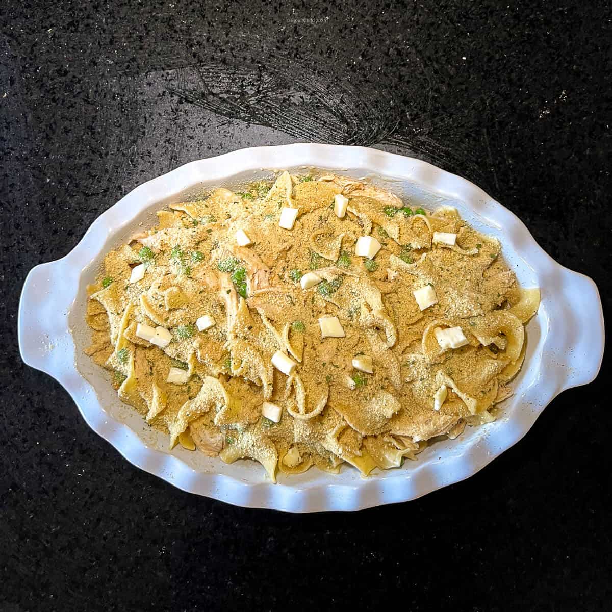 All ingredients added to casserole dish and topped with breadcrumbs and dots of butter, ready to bake.