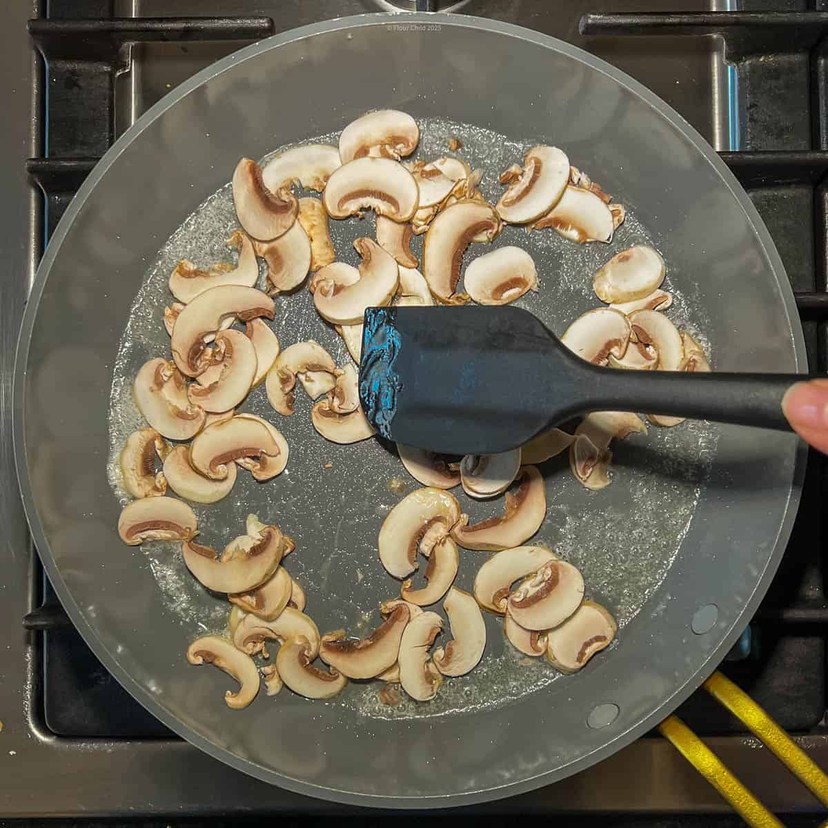 Mushrooms being sautéed in a deep fry pan and being stirred with a spatula.