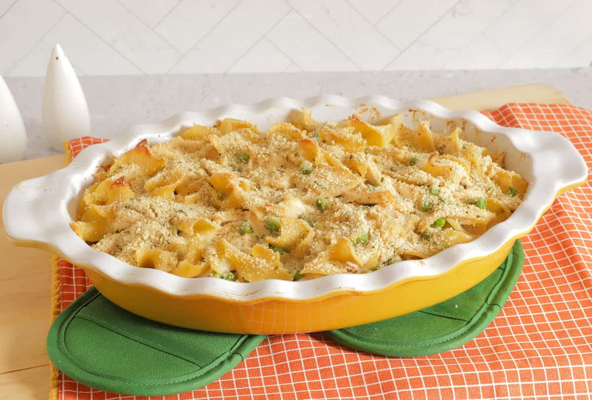 A gold casserole dish filled with Rock Hudson's chicken casserole on top of green hot pads and an orange towel.