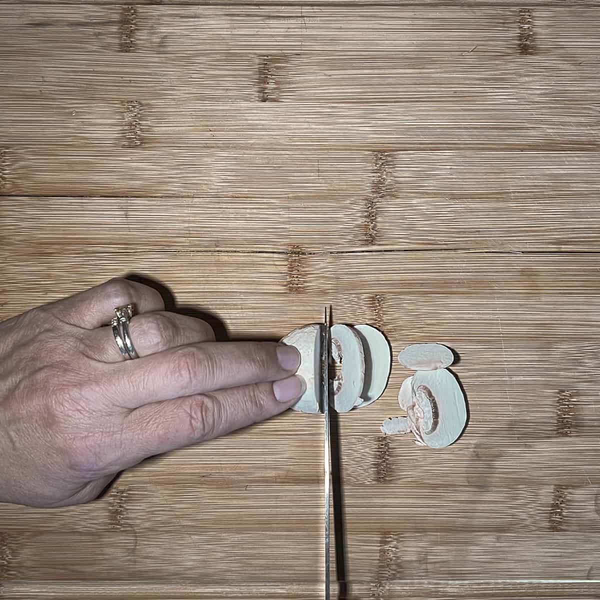 Slicing the mushroom caps on a cutting board after washing them.