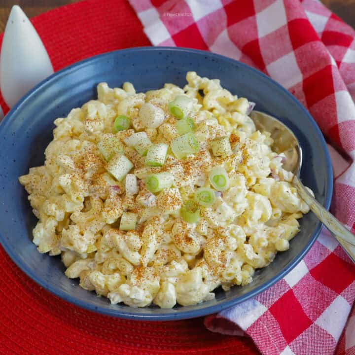 A blue serving bowl of deviled egg salad with a spoon in it, next to a red and white checkered napkin and salt and pepper shakers.