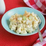 A blue serving bowl filled with deviled egg salad garnished with paprika and green onions on a red background.